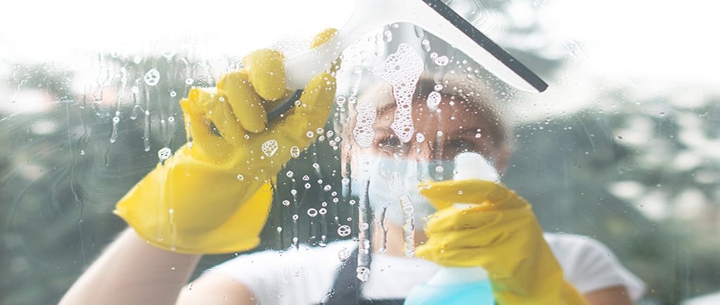 a woman in a black apron and yellow gloves cleaning a window
