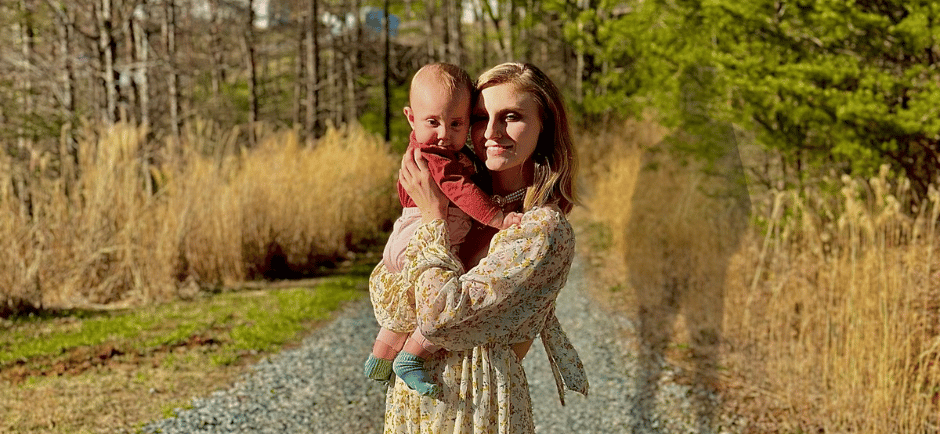A mother holding baby on a gravel road at dusk, with the shadow of the father looming behind—tension of co-parenting & abuse