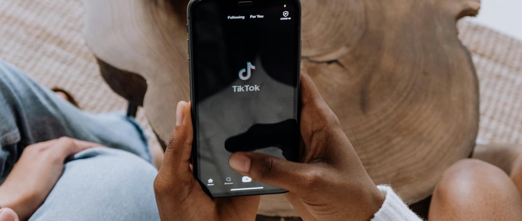 A person holding a smartphone showing the TikTok home screen, illustrating the cybersecurity risks o