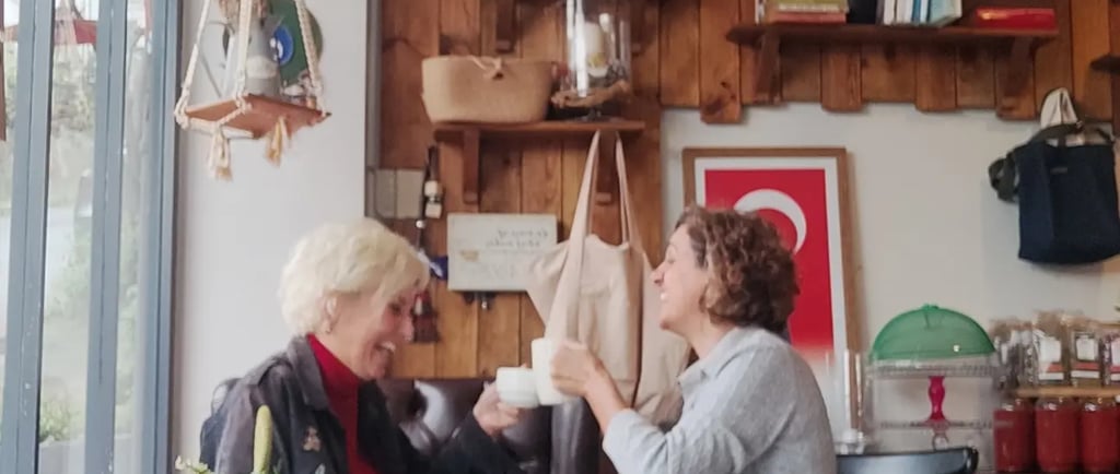 Two women emel and gülay talking and drinking coffee in a cozy rustic cafe with wooden wall decor.