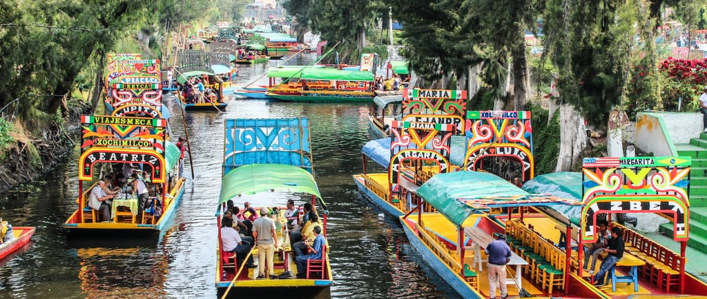 Colorful trajinera boats with tourists navigating the historic canals of Xochimilco in Mexico City.