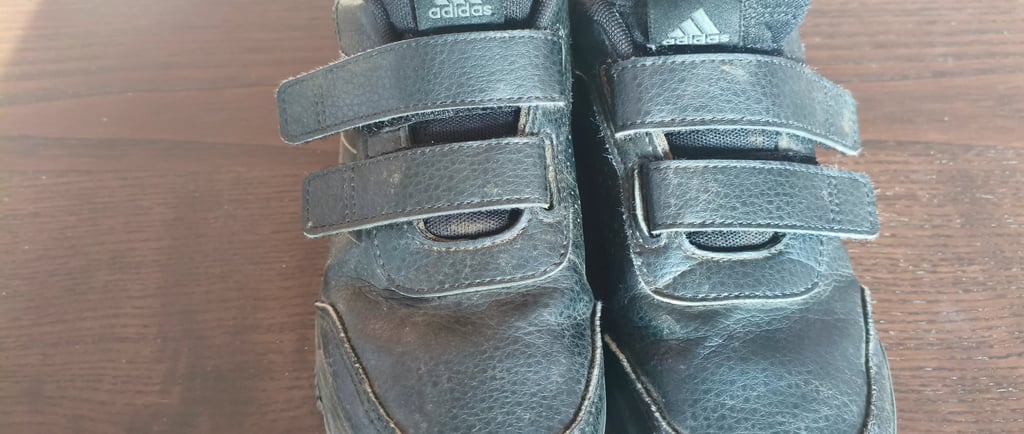 Análise detalhada do desgaste frontal e costuras em sapatilhas infantis pretas Adidas Tensaur com ve
