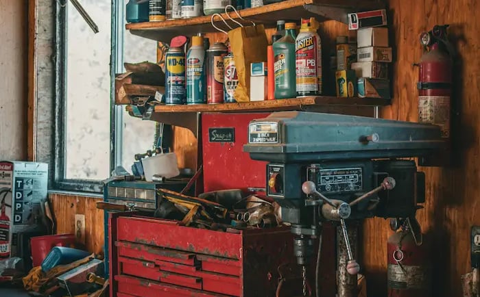 Rustic wood workshop workbench with a red metal toolbox, bench grinder, and drill press.