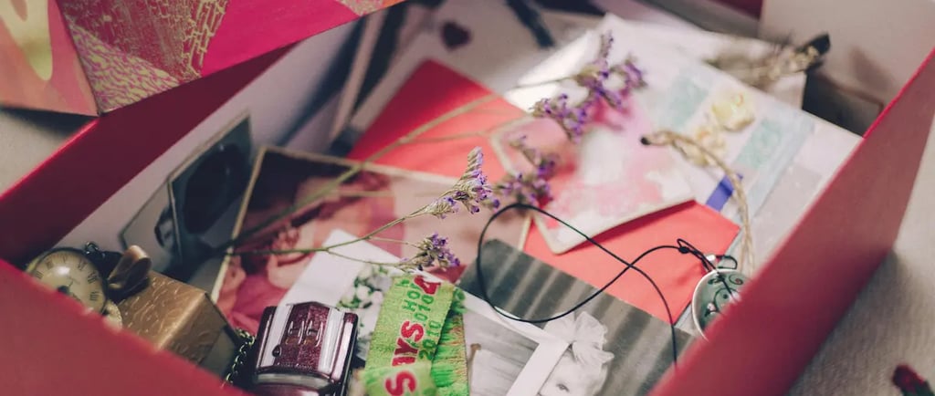 A red keepsake box filled with sentimental vintage photos, dried flowers, and small mementos.