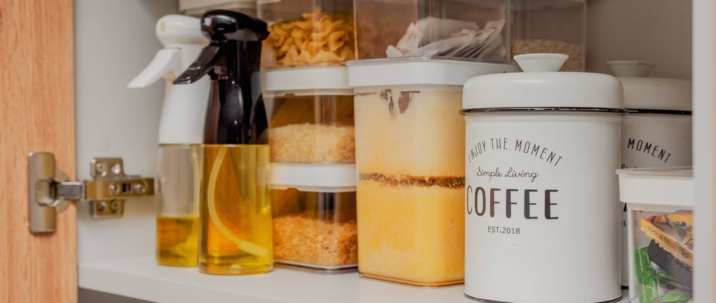 Kitchen cupboard with full storage canisters, oil spray bottles and beige coffee canister