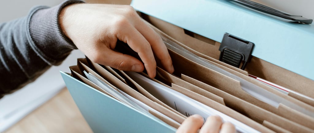 Man in grey jumper filing papers in a light blue expanding folder