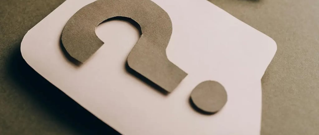 Two paper cutouts of question marks inside speech bubbles on a brown background representing help and FAQ.