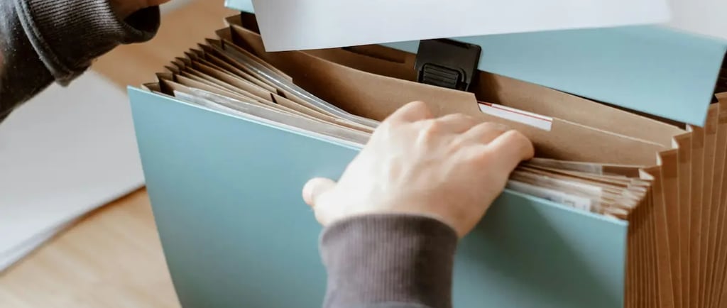 Person organizing paperwork in a blue expanding file folder for office document storage.