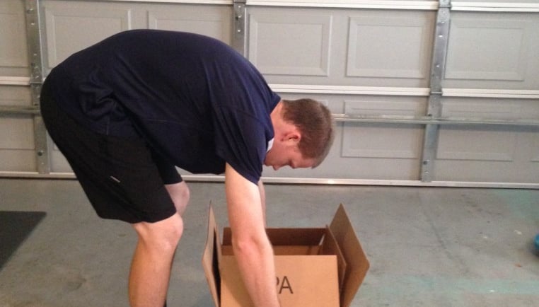 Pessoa abaixando objeto com tronco curvado, postura incorreta para coluna.