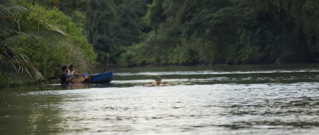 Local fisherman checking on the fish trap while the boy enjoys swimming