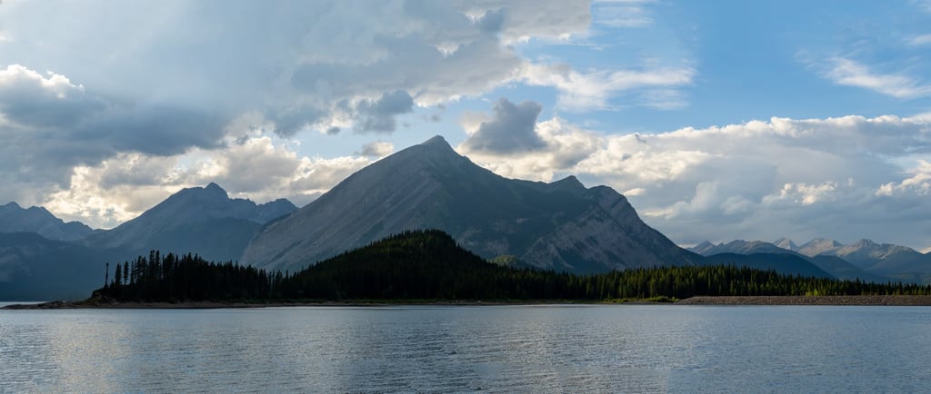 Wide panoramic view of Upper Kananaskis Lake with forested shoreline and Canadian Rockies peaks in P