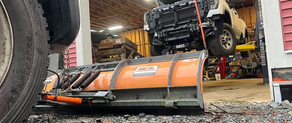 looking into a shop bay with a truck on a hoist from behind a plow blade