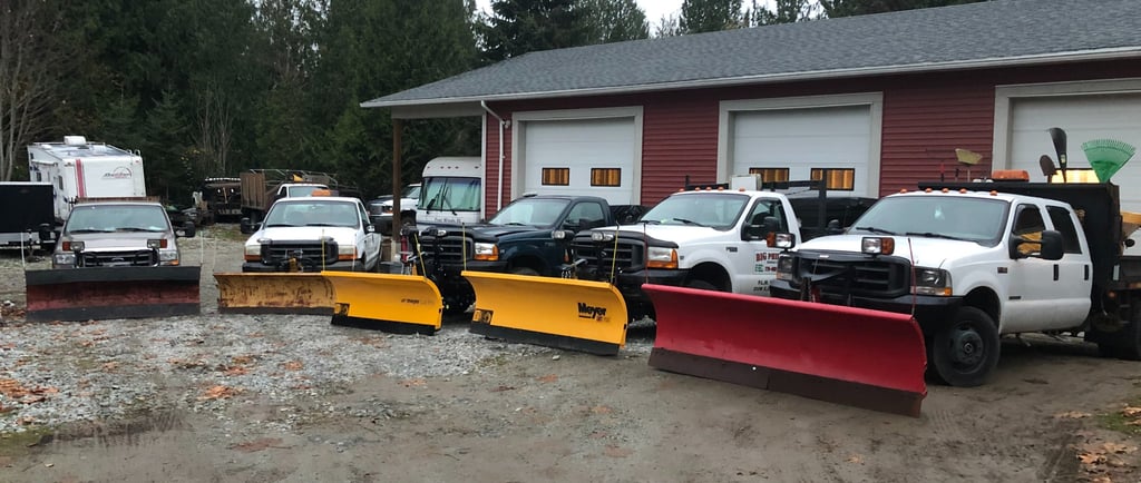 5 trucks with plows are parked in front of a 3 bay shop. The trucks are in a semi circle facing the camera