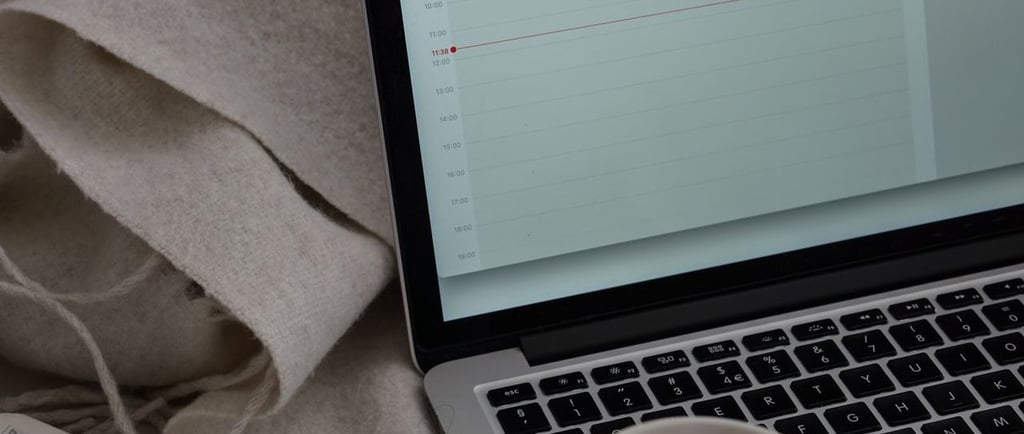 Notebook aberto sobre um sofá com calendário exibido na tela, ao lado de uma xícara de café e um cad