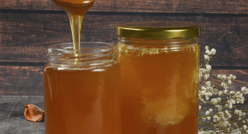 Pure organic honey dripping from a wooden spoon into glass jars on a rustic table.