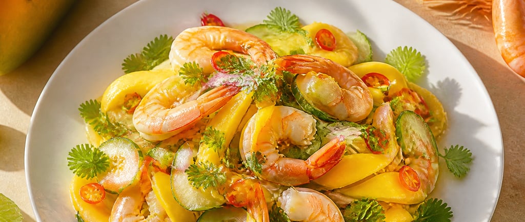 Thai shrimp and mango salad with cucumber, chili, and fresh mint on a white plate. with honey