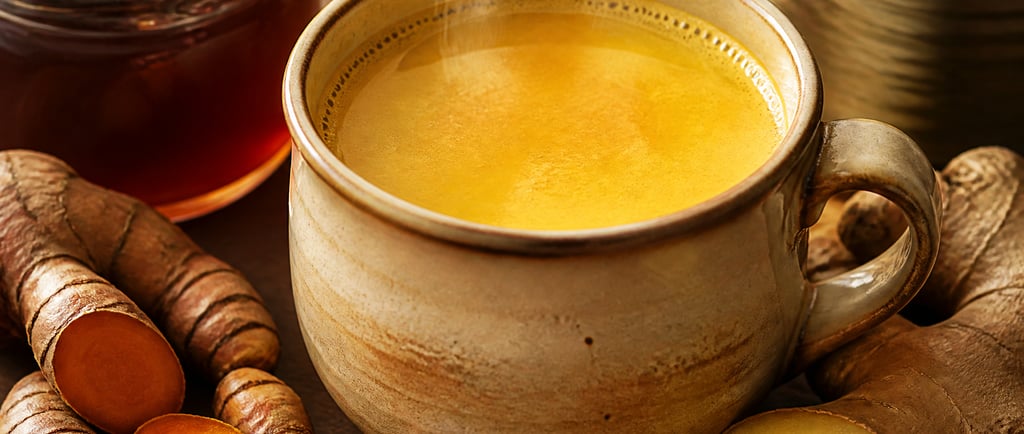 A steaming mug of golden turmeric milk latte with fresh turmeric root, ginger, honey, and cinnamon.