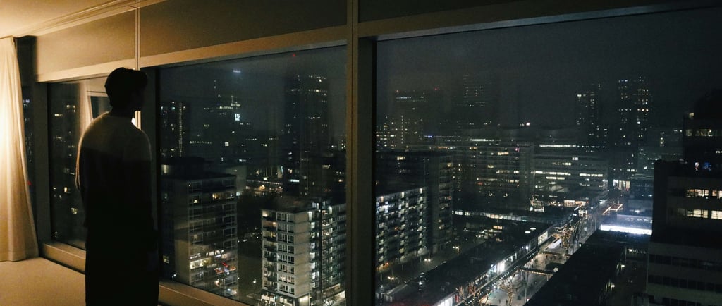 Silhouette of a person looking at the glowing city skyline and urban buildings at night through a large window.