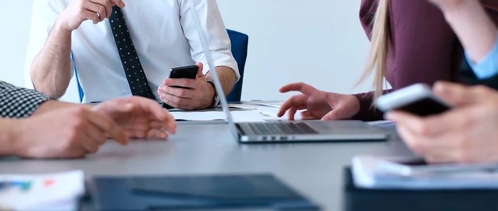 A manager using a smartphone during a professional meeting, illustrating distracted leadership.