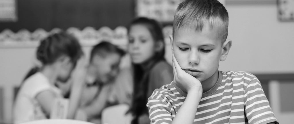 Chłopiec opierający głowę na dłoni, z poważnym, smutnym wyrazem twarzy i spuszczonym wzrokiem.