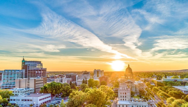 A golden sunset over the Boise, Idaho skyline featuring the State Capitol building and downtown city buildings.
