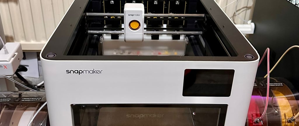 White Snapmaker J1 high-speed IDEX 3D printer with independent dual extruders on a workshop desk.