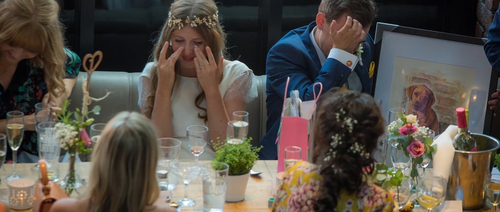 An emotional bride and groom crying during wedding speeches at a rustic reception table.