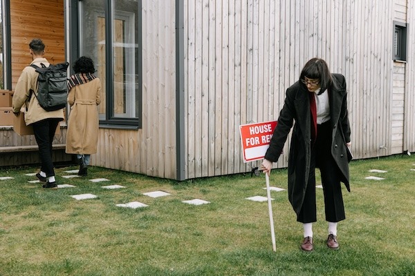 a woman removing for rent sign in front of a house
