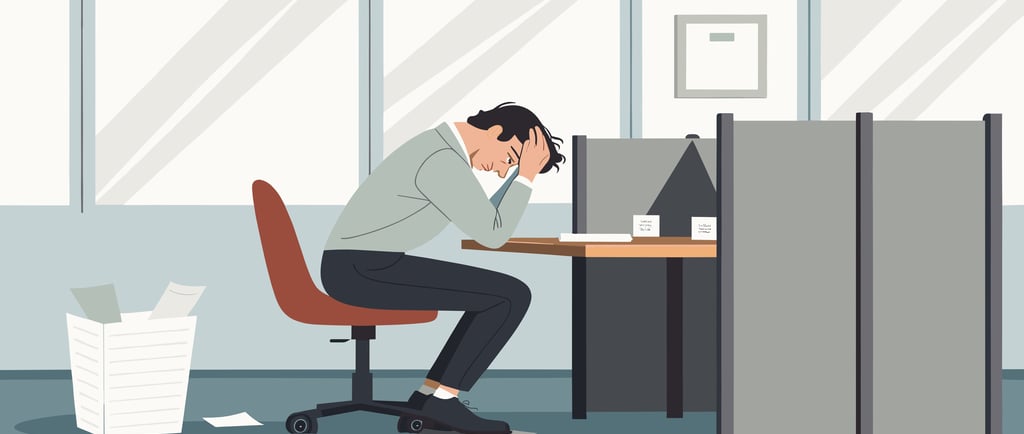 Stressed office worker sitting at a desk with head in hands, experiencing work burnout and stress.