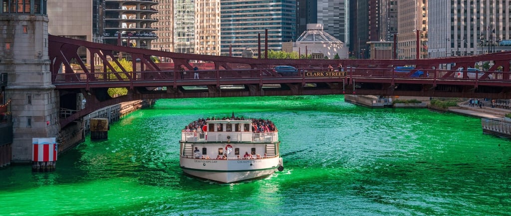 A white tour boat cruises on the bright green Chicago River under the Clark Street bridge.