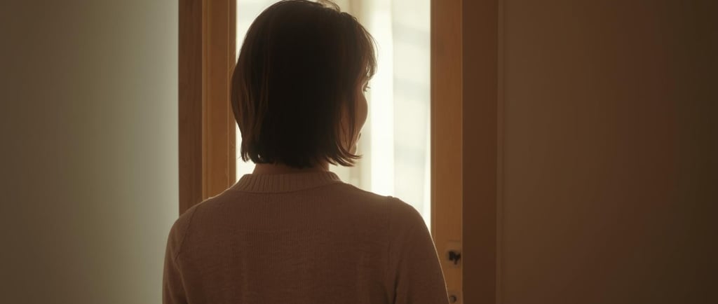 Back view of a woman with short brown hair looking through a doorway toward a bright light.