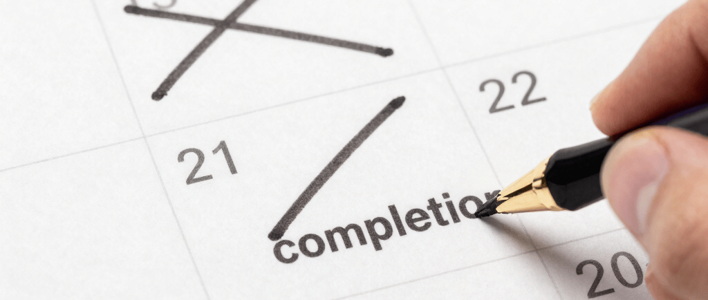 Hand writing completion on a paper calendar with a fountain pen to mark a project deadline.