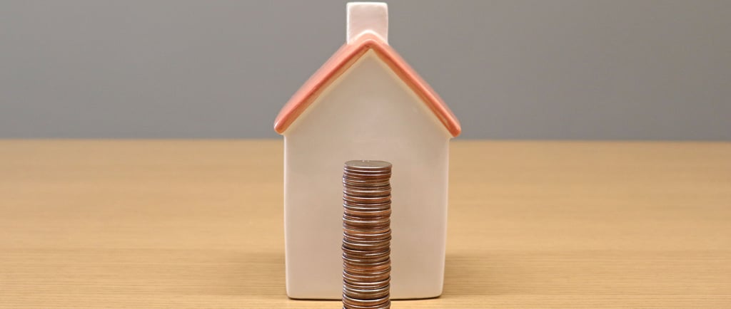 A stack of silver coins in front of a small ceramic house model representing real estate savings and mortgage payments.