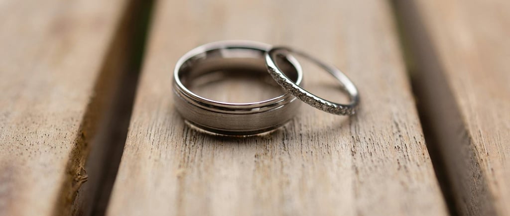 Elegant silver wedding bands, one plain and one diamond-studded, lie on rustic wooden planks, symbolizing marriage and