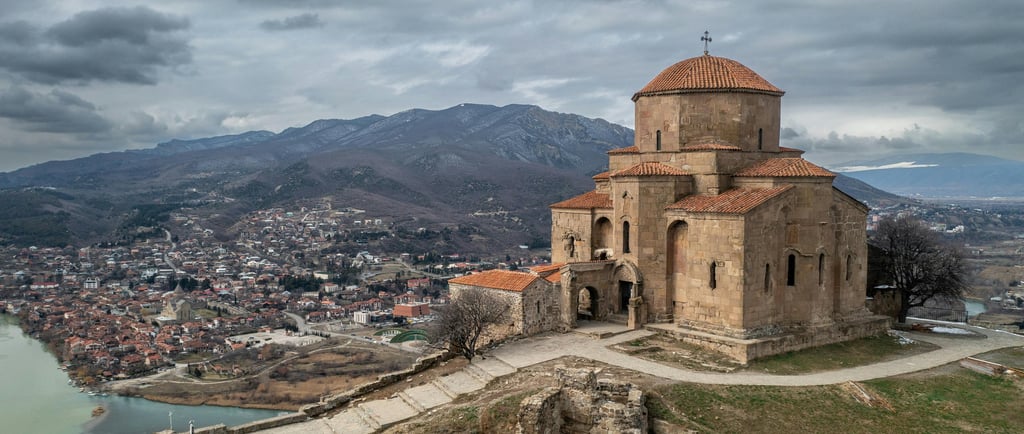 Ancient Jvari Monastery overlooking Mtskheta and the river confluence in Georgia under a cloudy sky.