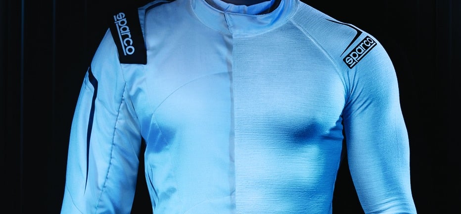 A driver wearing a white Sparco fireproof racing suit with visible shoulder patches and safety padding.