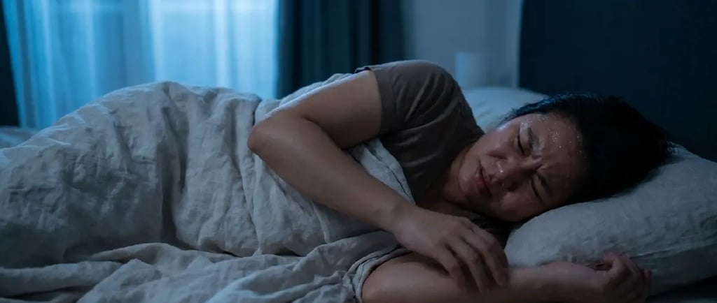 A sweating woman suffering from night sweats and sleep disturbance in a dark bedroom.