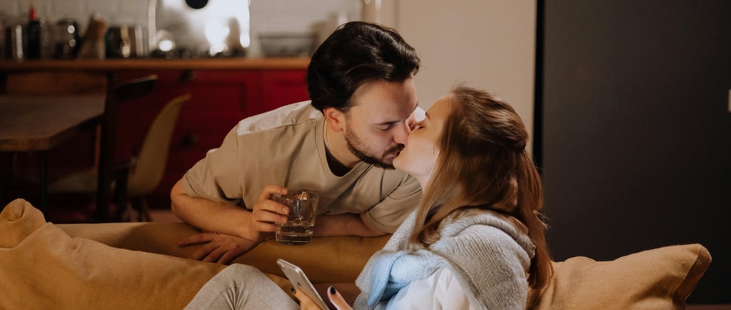 Happy couple sharing a romantic kiss while relaxing on a couch in a cozy home setting.