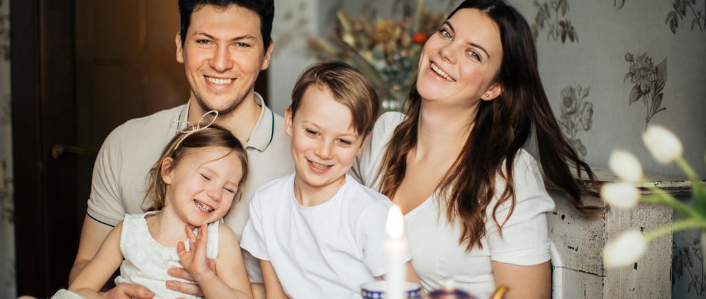 A happy family of four smiling together during a cozy tea time at home with vintage blue tea sets.
