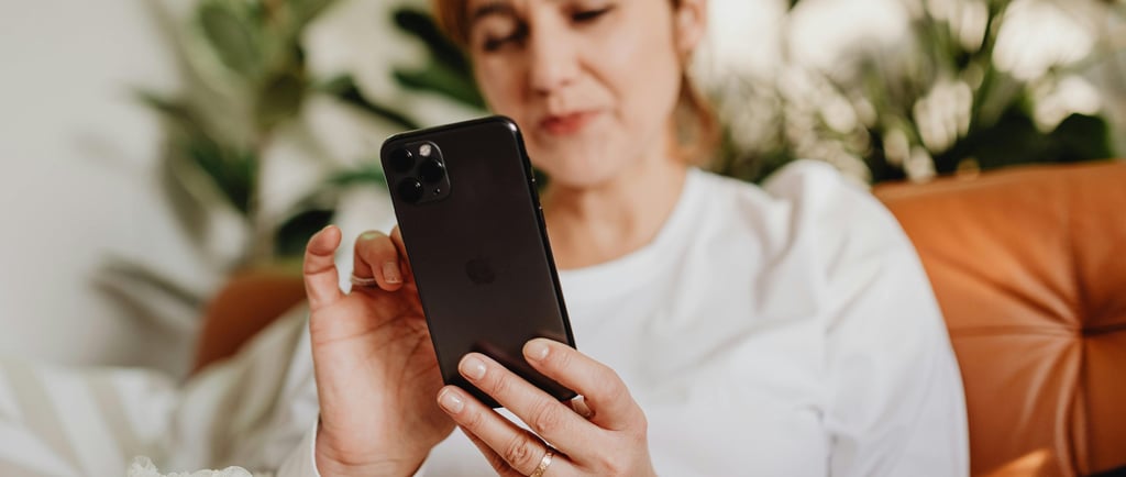 A woman relaxing on a leather sofa uses her smartphone with indoor plants in the background.