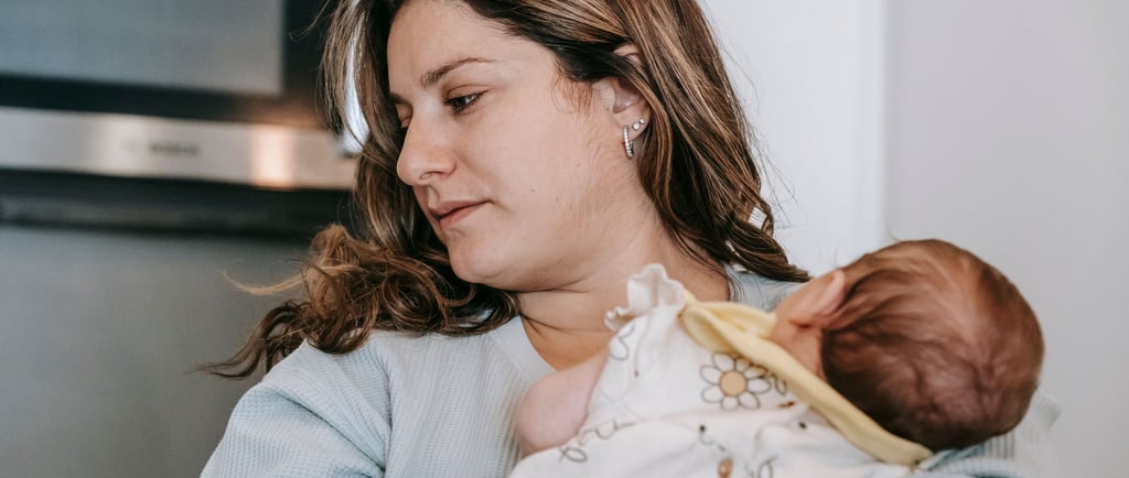 A mother holding her newborn baby at home in a kitchen setting, focusing on postpartum care.
