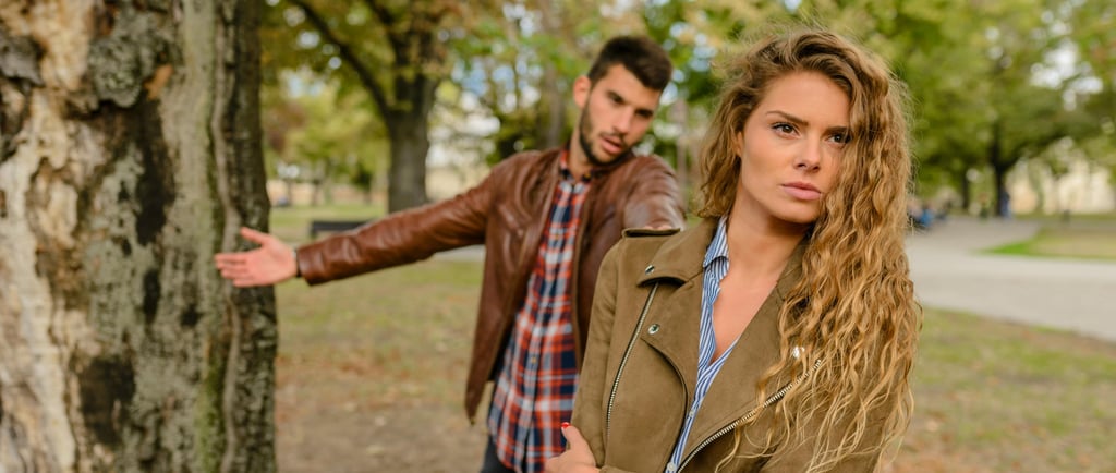 A young couple in a park having a relationship argument as the woman looks away frustrated.