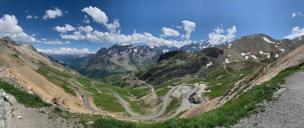 Kurvenreiche Passstrasse durch die französischen Alpen mit grünen Tälern und schneebedeckten Gipfel