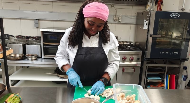 Chef Viviane in white chef jacket chopping mushrooms on a green board with a bowl and prep containers.