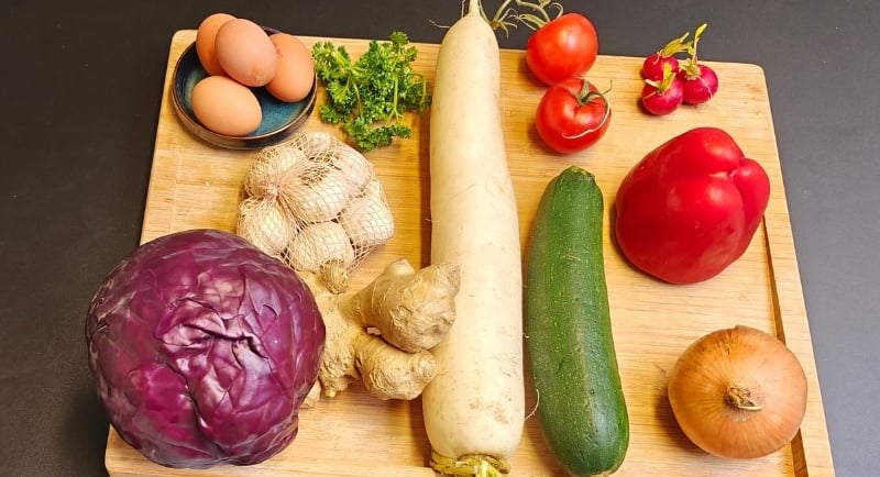 A variety of fresh vegetables including red cabbage, daikon radish, courgette, tomatoes, ginger and red pepper arranged.