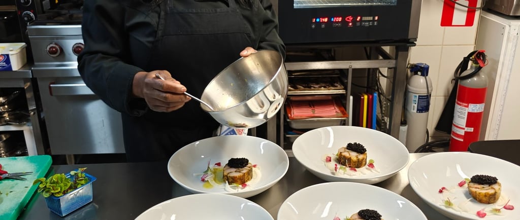 Chef Viviane spooning sauce over multiple fine dining plates lined up on a professional kitchen pass at klavertje vier.