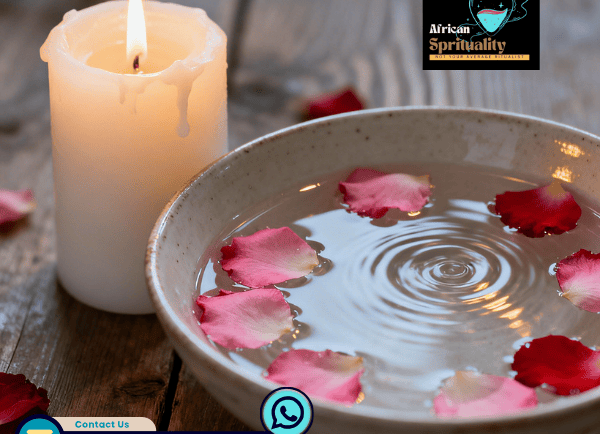 Spiritual cleansing bowl with pink rose petals in water next to a burning white candle.
