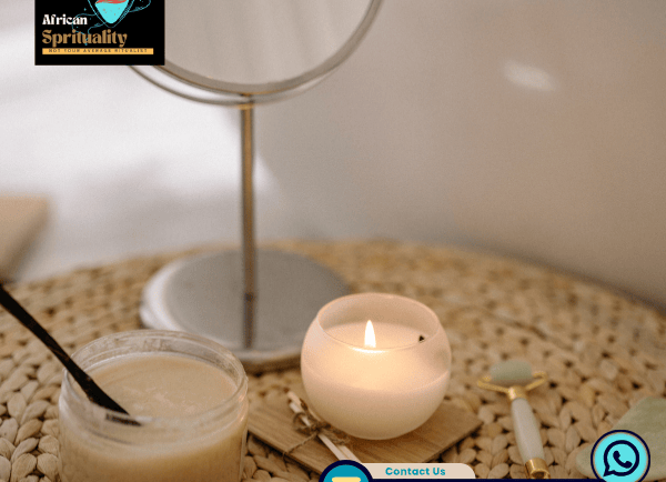 Lit white candle, spiritual body scrub, and jade roller on a woven mat for holistic wellness.