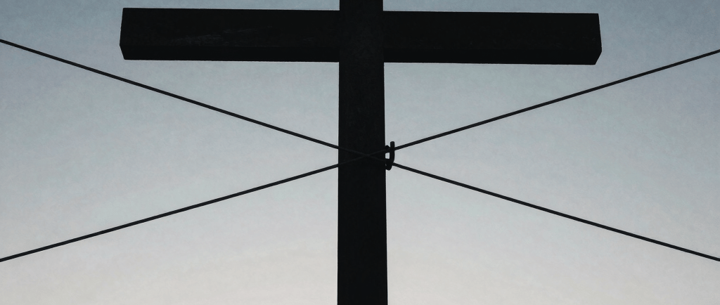 A silhouette of a large Christian cross against a blue and orange sunset sky.