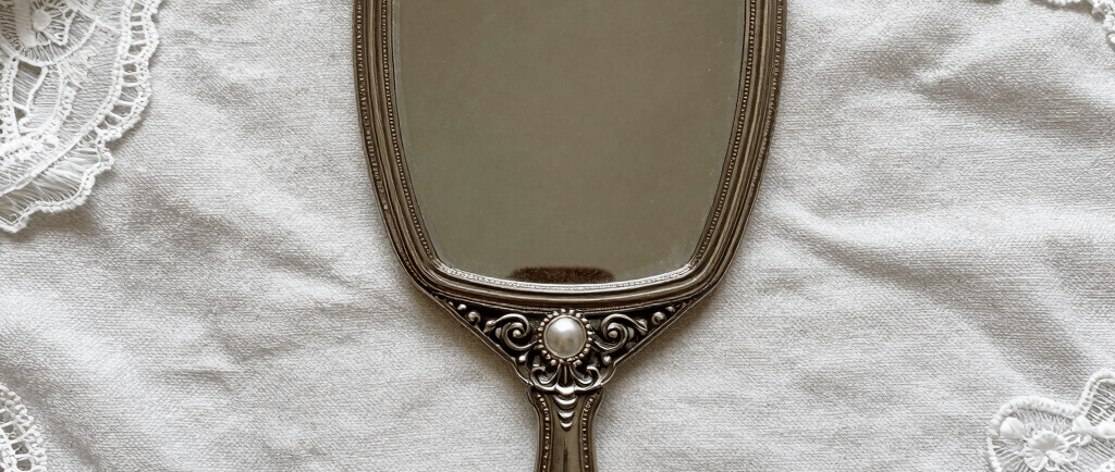 Vintage silver hand mirror with pearl accents on a white lace and linen background.